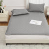 A gray waterproof mattress protector with elastic straps is placed on a bed, featuring a quilted surface and white padding.