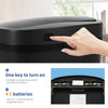 A hand is pressing a sensor on the lid of a black automatic touchless trash can.