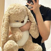 A person is holding a light tan long-eared rabbit plush toy close to their face.