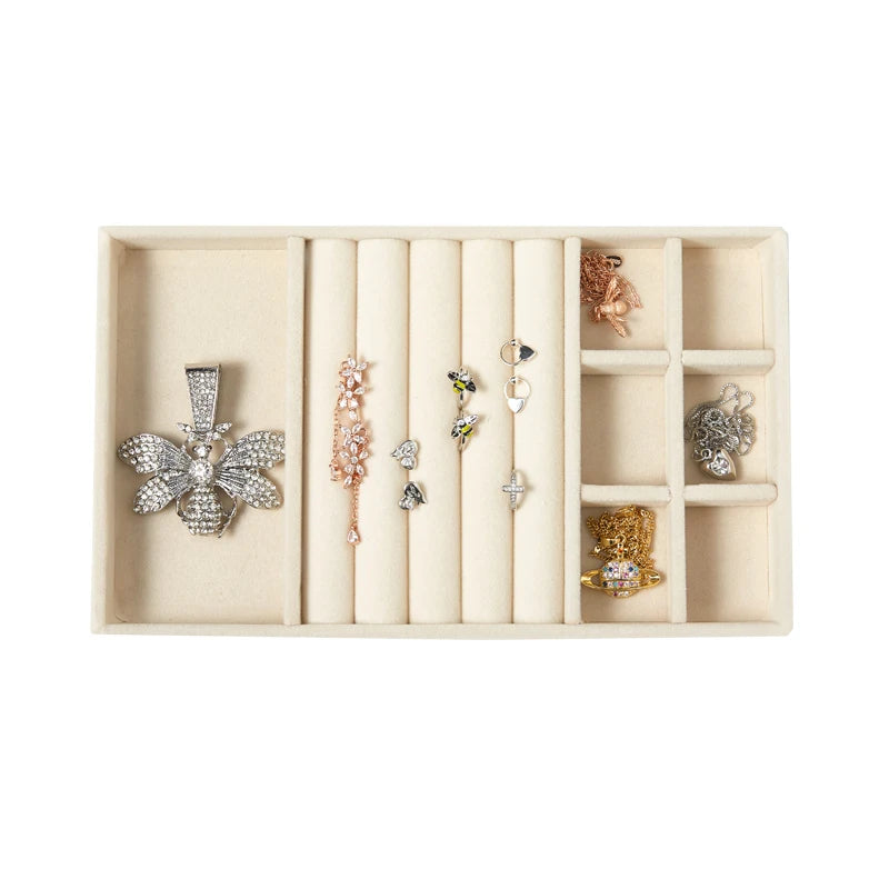 A light beige velvet jewelry organizer tray with multiple detachable compartments holding various silver and gold jewelry pie