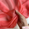 A hand is folding a piece of bright coral pink silk chiffon fabric to show its drape and texture.