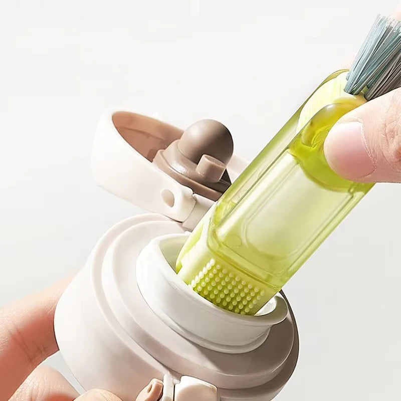 A hand is holding a light green multi-purpose cleaning brush set designed for bottles, cups, and straws.