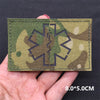 A rectangular olive green tactical patch featuring a dark gray medical cross design on a dark fabric background.