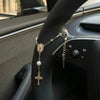 A gold rosary necklace with a pearl pendant is displayed on the steering wheel of a car.