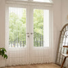 White bohemian tassel curtain with lanterns covering a glass door and window.