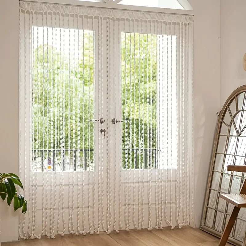 White bohemian tassel curtain with lanterns covering a glass door and window.