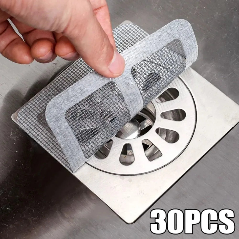 A hand is placing a disposable drain hair catcher sticker onto a metal drain grate.