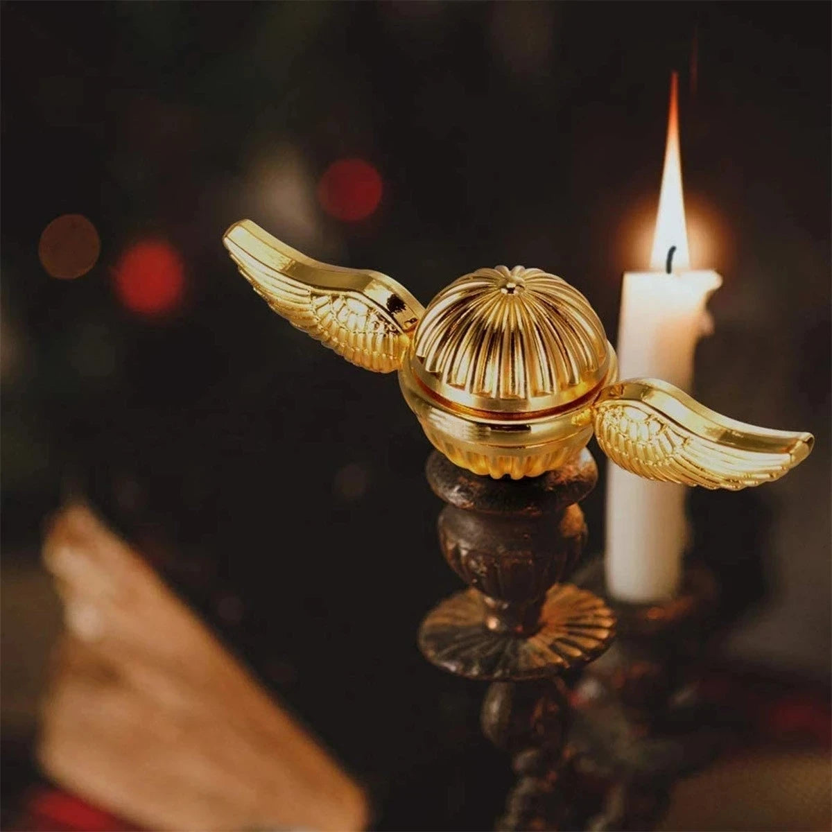 Golden snitch angel wings metal fidget spinner resting on a candle