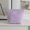 Pochette en crochet à rayures violettes et blanches posée sur une surface blanche à côté d'un tableau encadré.