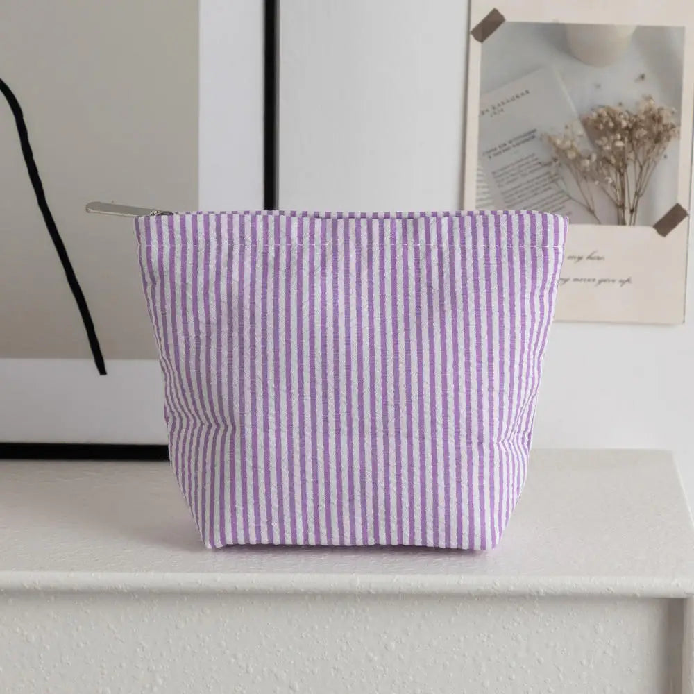 Pochette en crochet à rayures violettes et blanches posée sur une surface blanche à côté d'un tableau encadré.