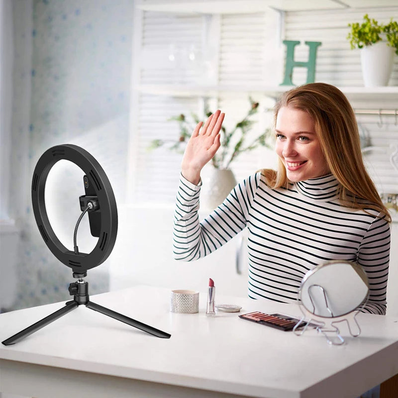 A woman smiling while using a 33cm selfie ring light with a tripod stand on a white table.
