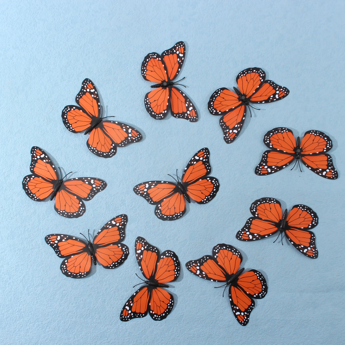 A collection of ten orange and black monarch butterfly magnets scattered on a light blue surface.