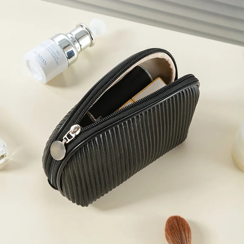 A black PU leather makeup bag with a zipper and a white cosmetic tube is shown on a light surface.