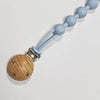 A silicone pacifier clip with a teether, featuring light blue spherical beads and a wooden disc.
