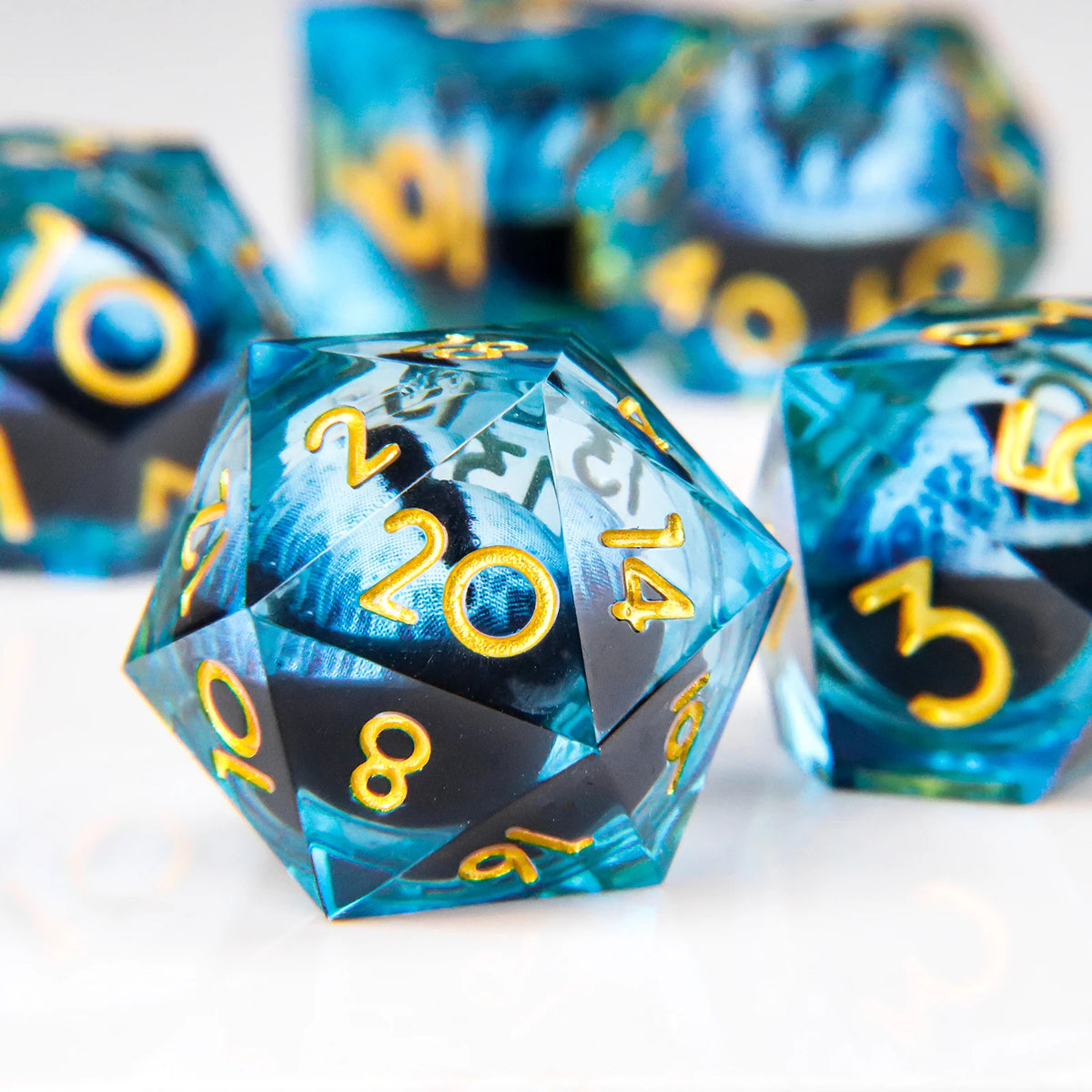 A close-up of a set of blue and black liquid core resin dice with gold numbering and dragon eye designs.