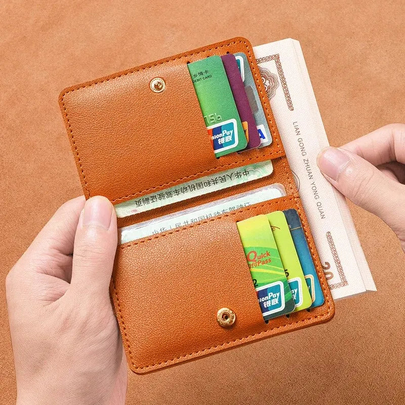 A brown leather compact wallet is shown open, displaying various cards and currency against a tan background.
