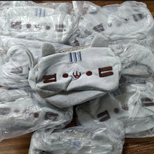 A pile of cute cat plush pencil cases with zipper closures in light gray fabric, packaged in clear plastic bags.