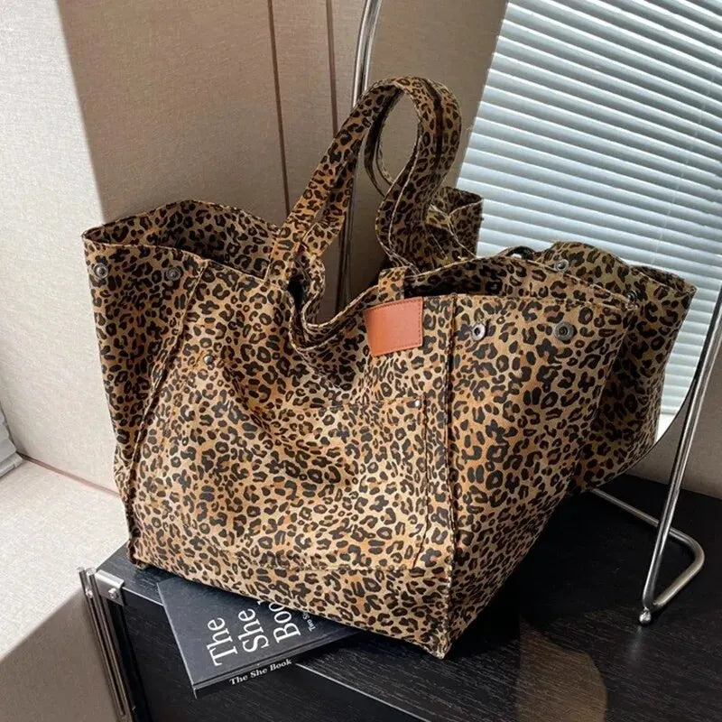 A brown leopard print canvas tote bag resting on a dark surface next to a book.
