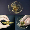A close-up of a golden metal fidget spinner shaped like angel wings rotating on a glass surface.