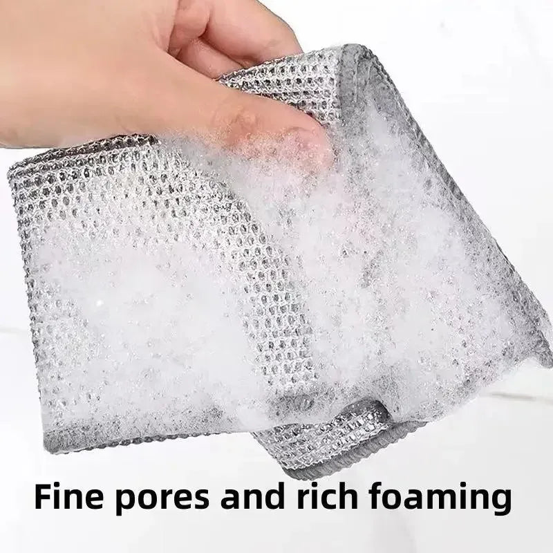 A hand is squeezing a gray, mesh cleaning cloth that is producing rich white foam.