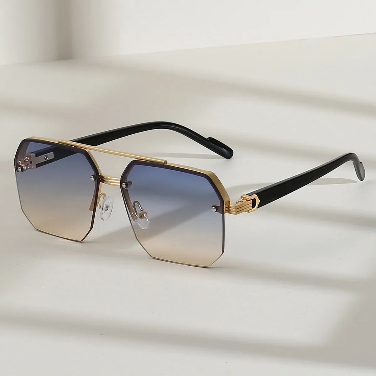 Lunettes de soleil rétro carrées à moitié cadre en métal avec accents dorés et branches noires, posées sur une surface blanch