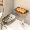 A silver aluminum wall-mounted soap dish with a drain and an orange bar soap resting on it.