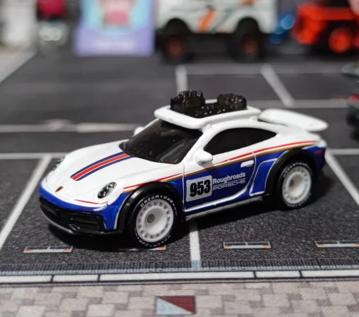 A white and blue die-cast model car, resembling a Porsche, is displayed on a black grid surface.