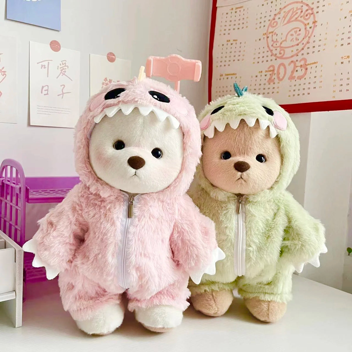 Two plush teddy bear dolls wearing dinosaur jumpsuits, one pink and one green.