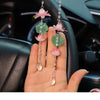 A hand holds several pink lotus car pendants featuring green leaves and clear beads against a dark car interior background.
