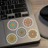 A laptop shows a collection of colorful mandala and graffiti stickers on its surface.