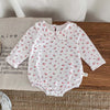 White long-sleeved baby girl floral lace cotton romper with a Peter Pan collar lying on a wooden surface.