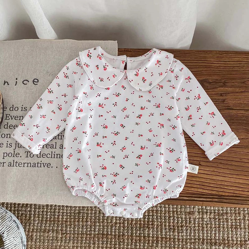 White long-sleeved baby girl floral lace cotton romper with a Peter Pan collar lying on a wooden surface.