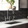 A kitchen sink and countertop with a modern faucet set against a dark gray herringbone tile backsplash.