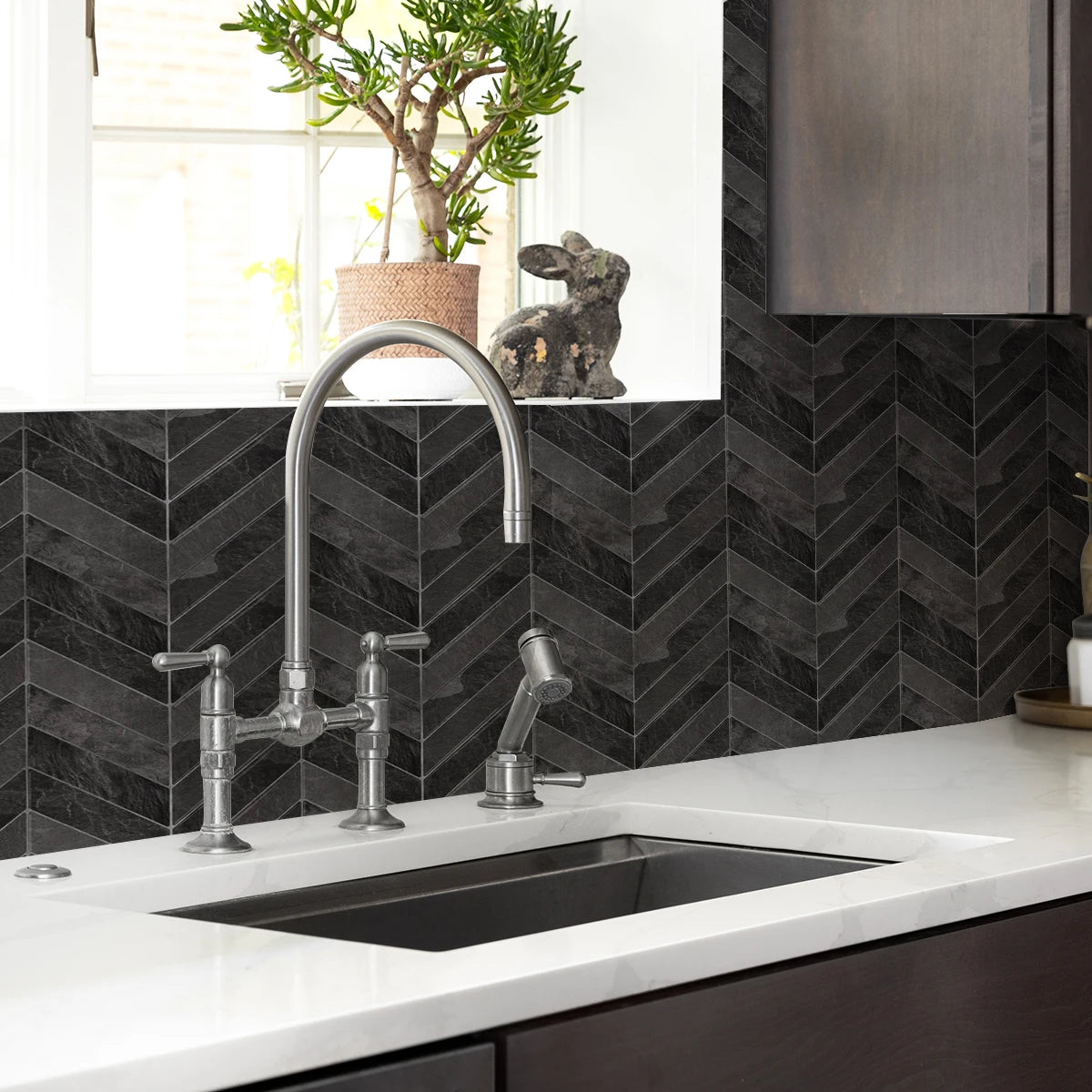 A kitchen sink and countertop with a modern faucet set against a dark gray herringbone tile backsplash.