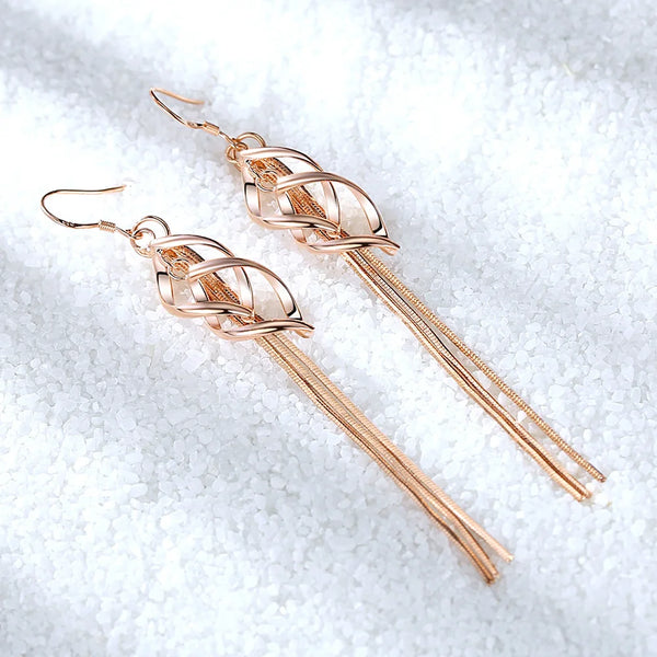 Boucles d'oreilles en anneaux dorés délicats avec un motif ondulé entrelacé sur une surface blanche et enneigée.