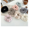 A collection of soft, plush coil hair ties in various shades of pink, gray, and black are displayed on a white surface.