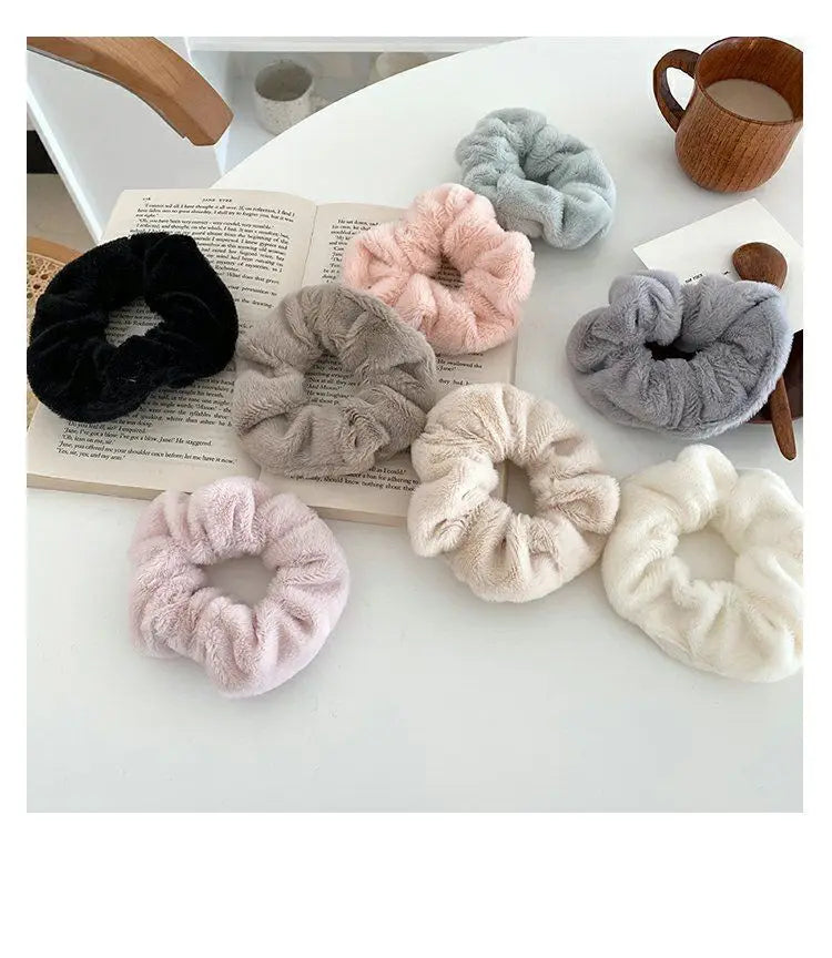 A collection of soft, plush coil hair ties in various shades of pink, gray, and black are displayed on a white surface.