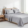 A set of four striped satin bed sheets in gray are displayed on a wooden bed with pillows and bedding.