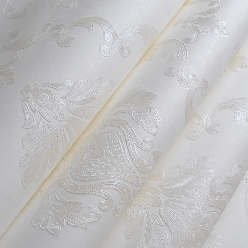 A close-up of an embossed damask wallpaper roll featuring delicate floral and scroll designs on white fabric.