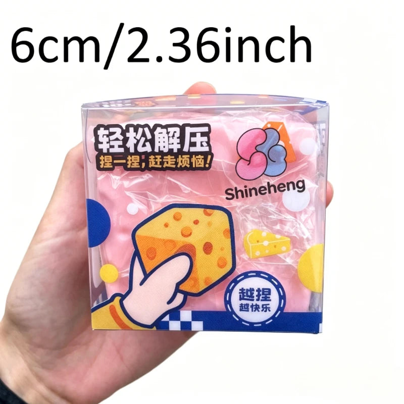 Eine Hand hält einen durchsichtigen Plastikbehälter mit einem rosa, weichen Käse-Fidget-Spielzeug mit gelben und orangen Akze