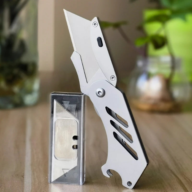 A white stainless steel folding utility knife with a visible blade is shown next to its protective sheath.