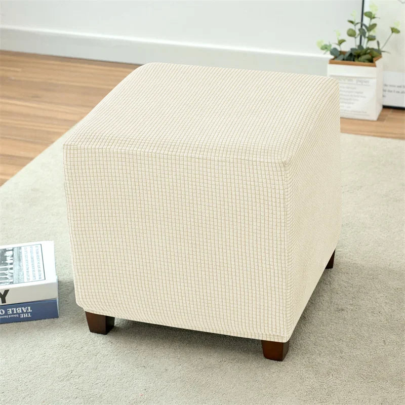 A beige, upholstered cube-shaped floor sofa cover with a quilted texture resting on a light carpet.