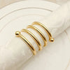 A set of twelve gold decorative metal napkin rings with a hollow-out pattern displayed on a white plate.