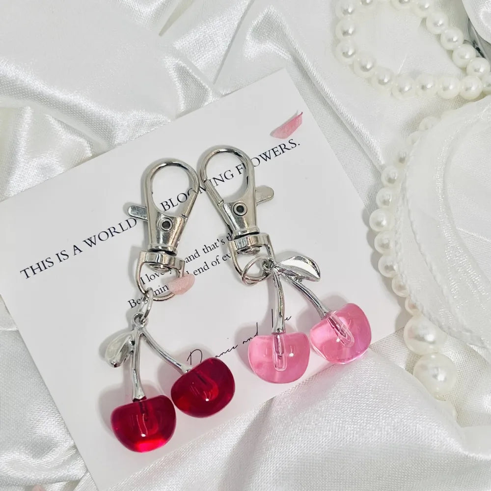 Un ensemble de clés en forme de cerises scintillantes roses et rouges, présentées sur une carte blanche avec un fond satiné.
