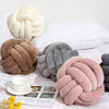 A collection of handmade knitted velvet throw pillows in shades of beige, brown, and gray resting on white bedding.