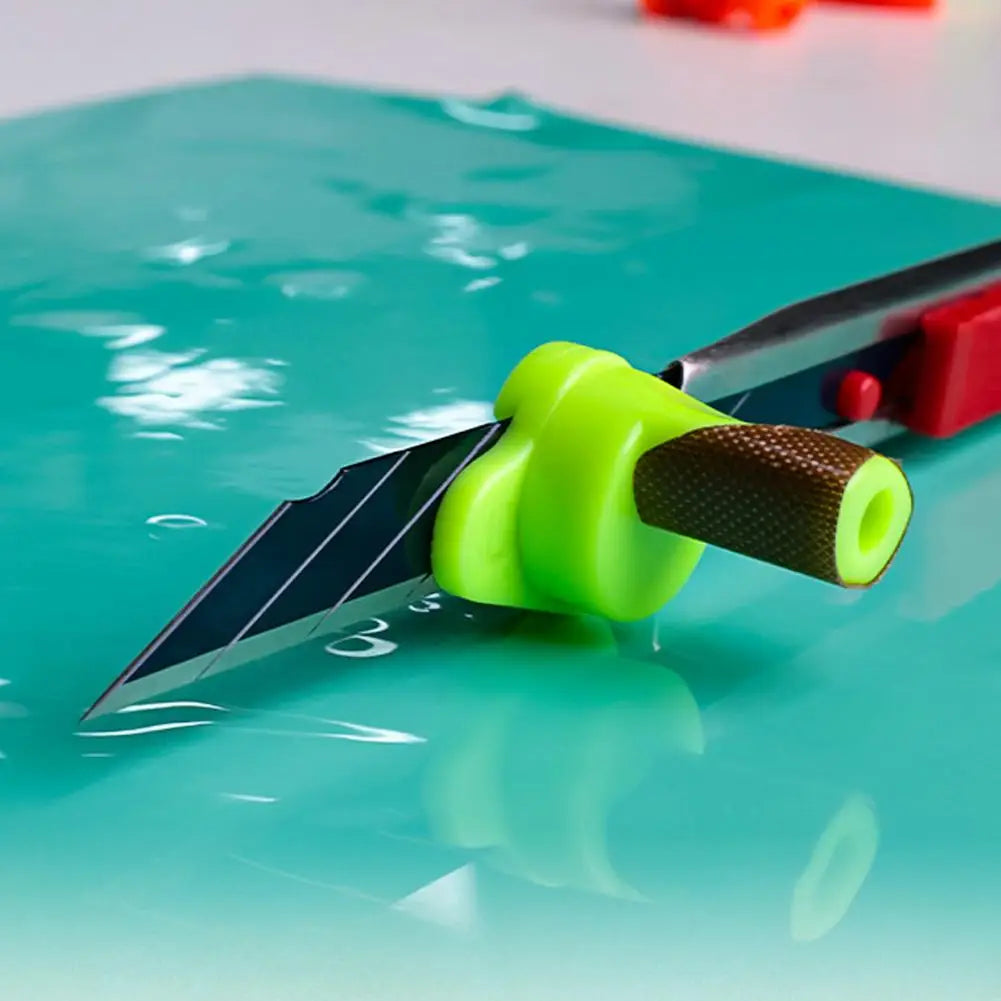 A bright green magnetic film cutting guide with a sharp blade is shown resting on a teal surface.