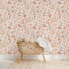 A woven wicker chair with a white blanket is placed against a vintage floral peel-and-stick wallpaper background.