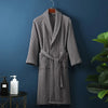 A gray lightweight cotton waffle robe hanging on a dark blue wall next to a potted green plant.