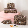 A pink and black leopard print toiletry bag set with a matching pink suitcase and grooming tools.