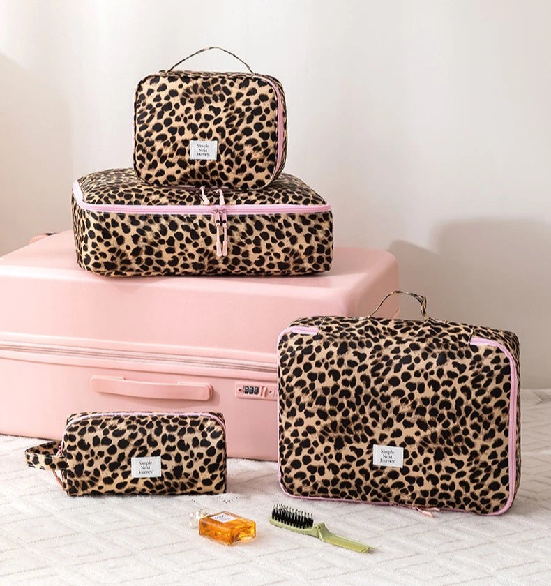 A pink and black leopard print toiletry bag set with a matching pink suitcase and grooming tools.
